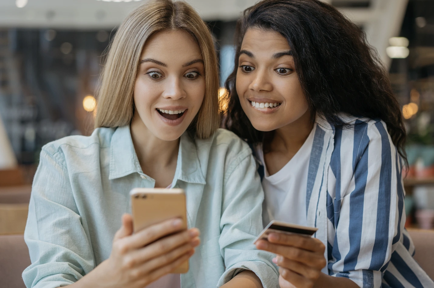 Two women looking at their mobile phones. The women are excited by what they see on their mobile phones